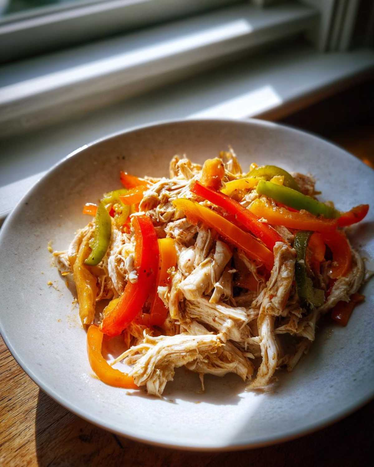 Shredded chicken mixed with strips of red, orange, and green peppers, ready for crockpot chicken fajitas.