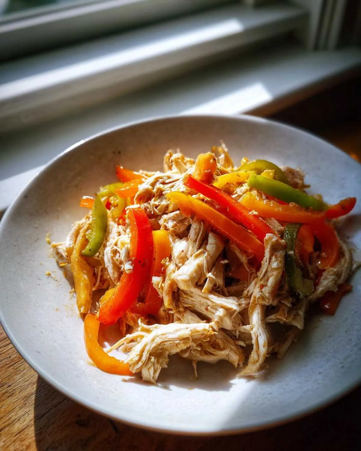 Shredded chicken mixed with strips of red, orange, and green peppers, ready for crockpot chicken fajitas.