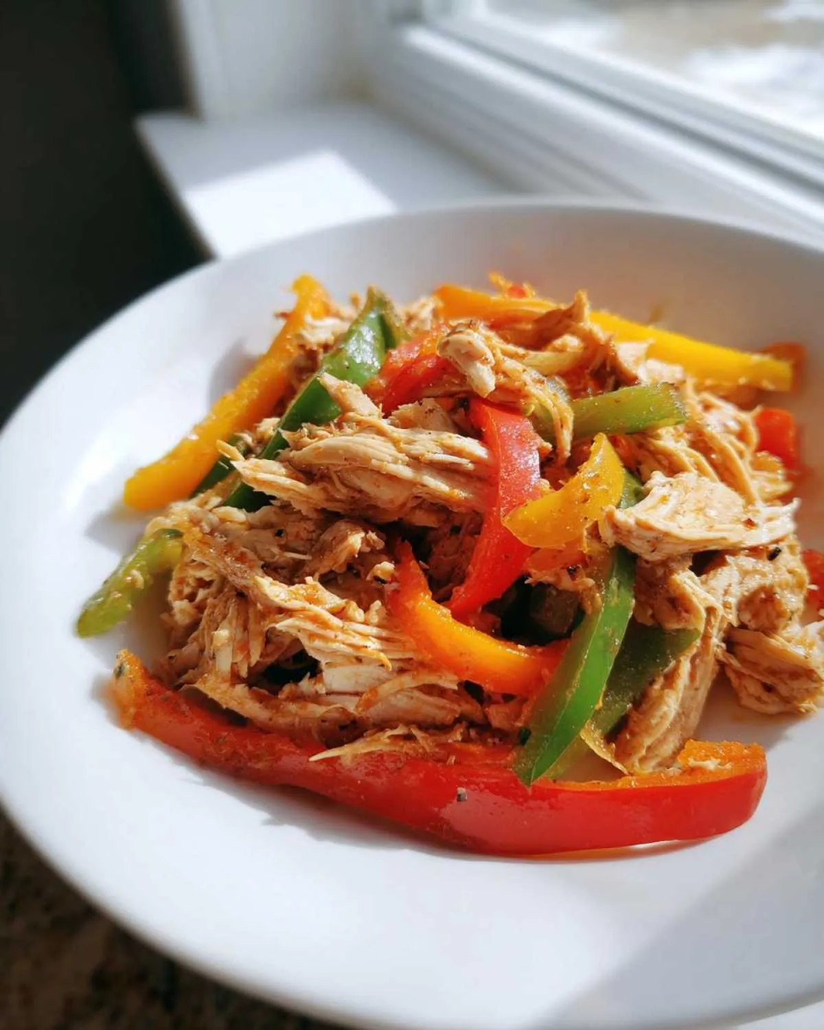 Shredded chicken mixed with sliced red, green, and yellow peppers, ready for crockpot chicken fajitas.