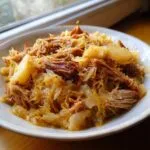 Close-up of a hearty serving of shredded pork and sauerkraut in a white bowl, ready to eat.
