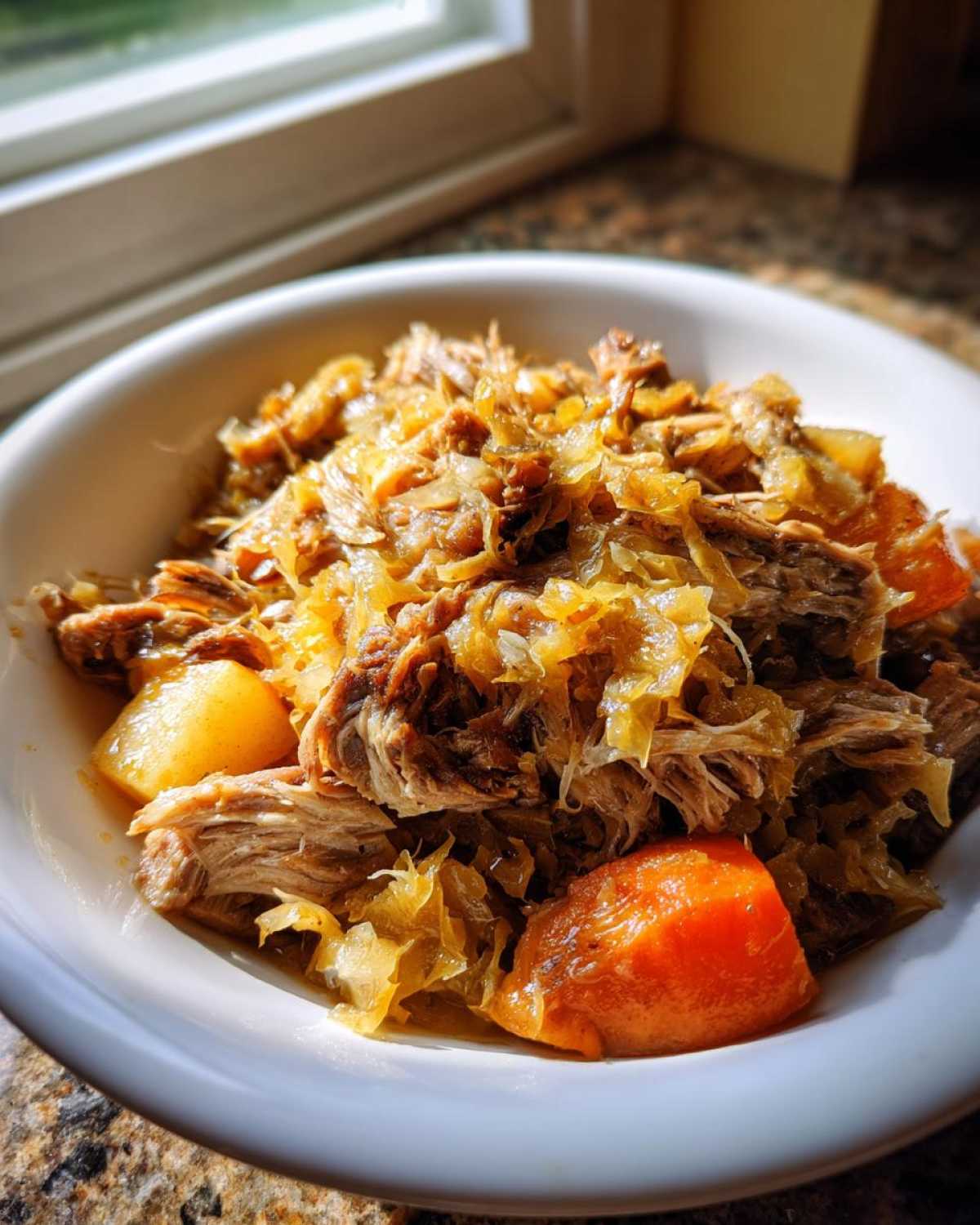 A close-up of shredded pork and sauerkraut mixed with chunks of carrots in a white bowl, featuring the pork and sauerkraut.