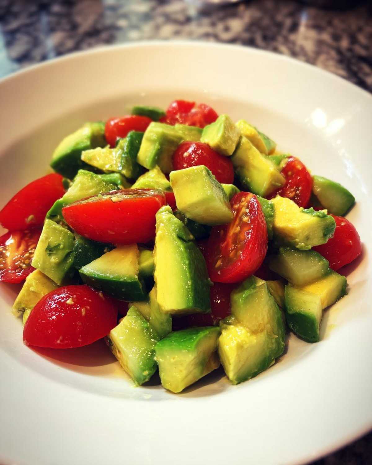 Close-up of a vibrant avocado salad featuring diced avocado and halved cherry tomatoes in a white bowl.