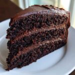 A moist, dark slice of chocolate fudge cake with three layers and thick fudge frosting.