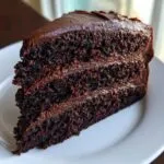 A moist, dark slice of chocolate fudge cake with three layers and thick fudge frosting.