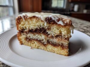 A moist slice of sour cream coffee cake with cinnamon swirl layers and white glaze drizzled on top.