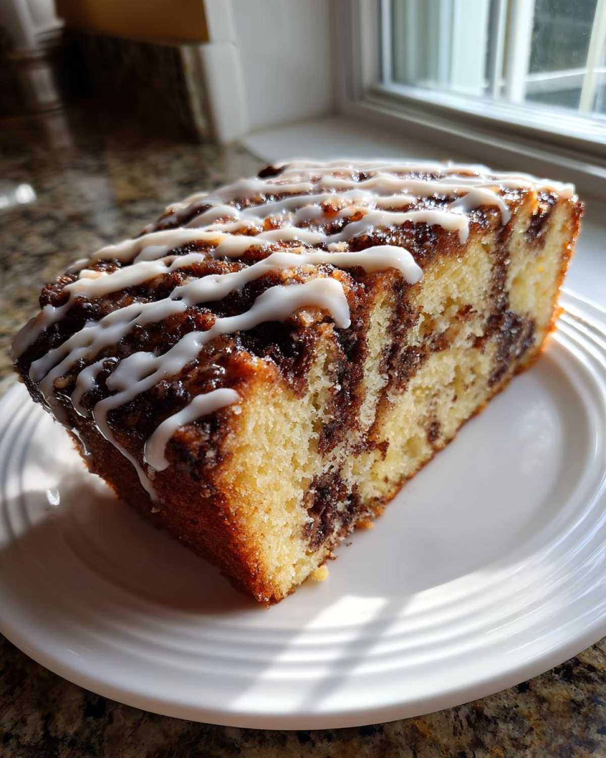 A close-up of a moist slice of sour cream coffee cake with a cinnamon swirl and white glaze drizzle.