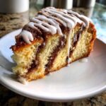 Close-up of a moist slice of sour cream coffee cake featuring a cinnamon swirl and drizzled with white vanilla icing.