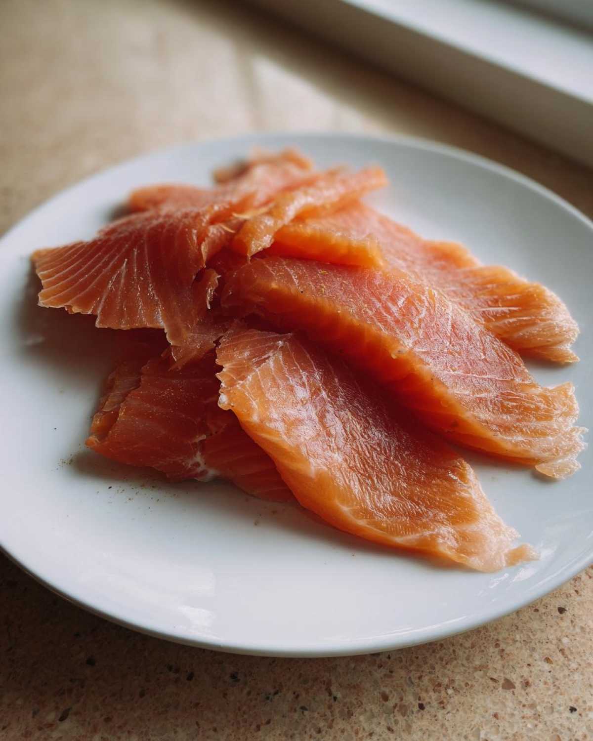 Close-up of thinly sliced, vibrant orange smoked salmon pieces arranged on a white plate.