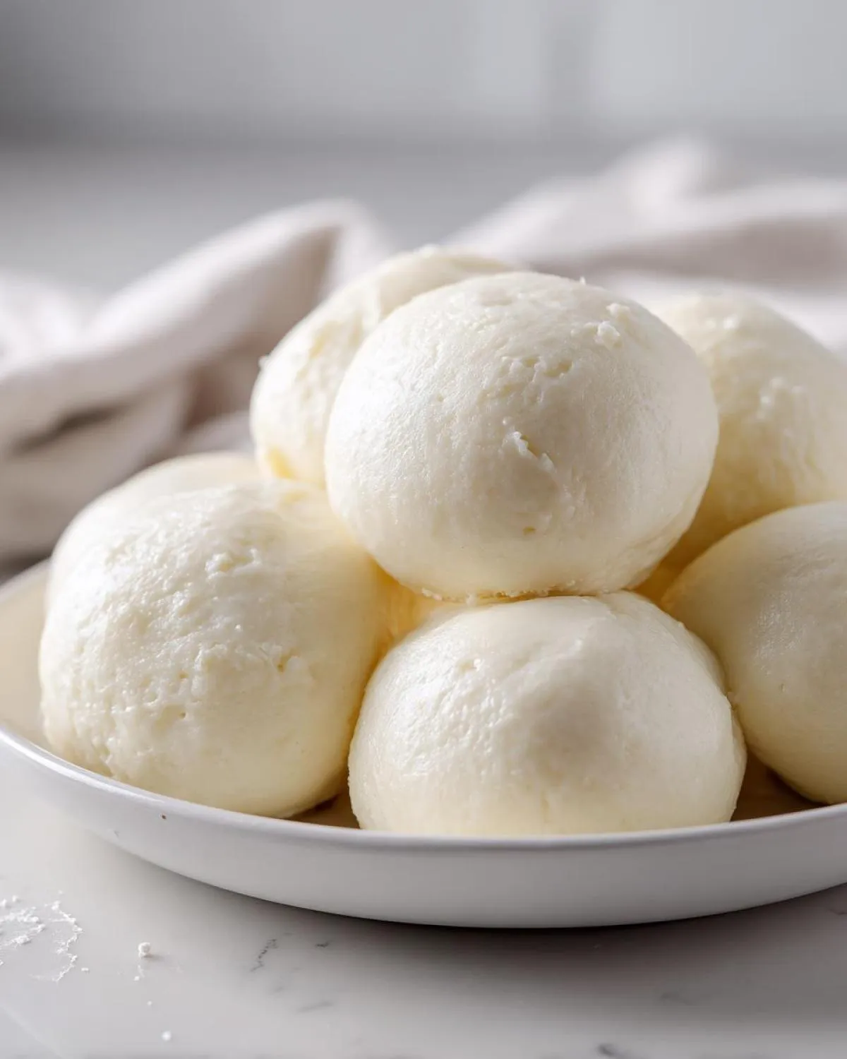 A close-up of several smooth, white balls of fufu stacked in a white bowl.
