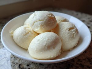 Close-up of five scoops of smooth, pale yellow fufu served in a white bowl.