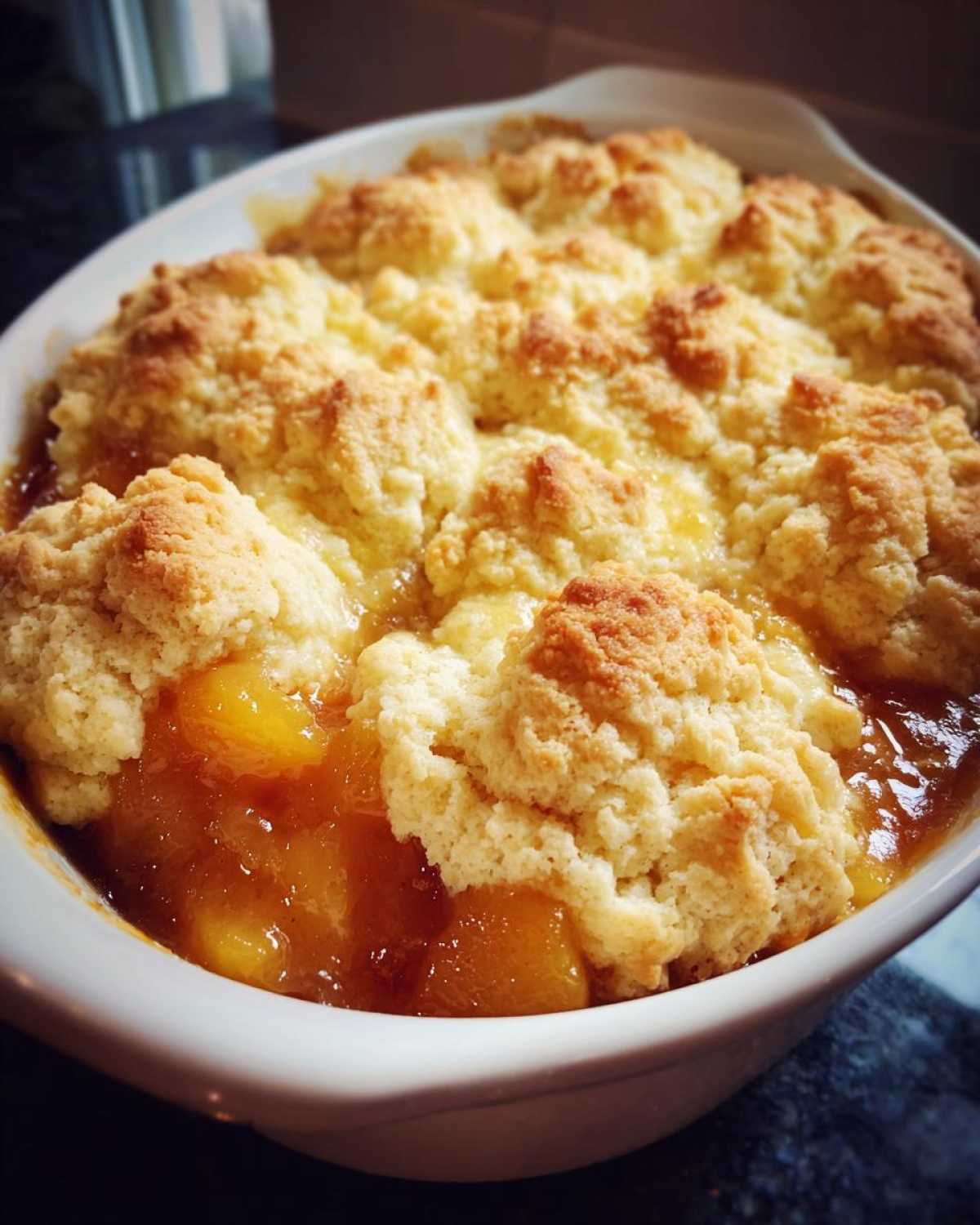 Close-up of a freshly baked southern peach cobbler with golden, biscuit-like topping bubbling over sweet peach filling.