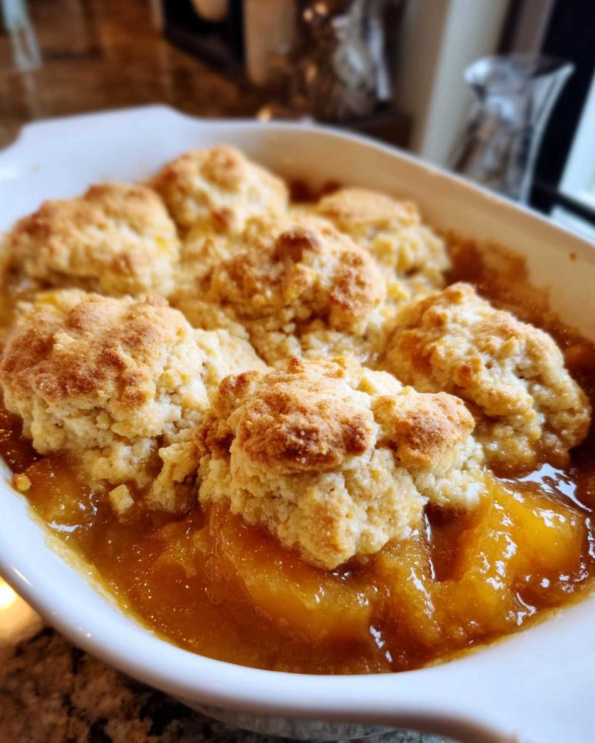 Close-up of a bubbling southern peach cobbler with golden biscuit topping in a white baking dish.