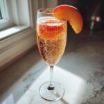 A refreshing, fizzy bellini recipe cocktail in a champagne flute, garnished with a fresh peach slice.