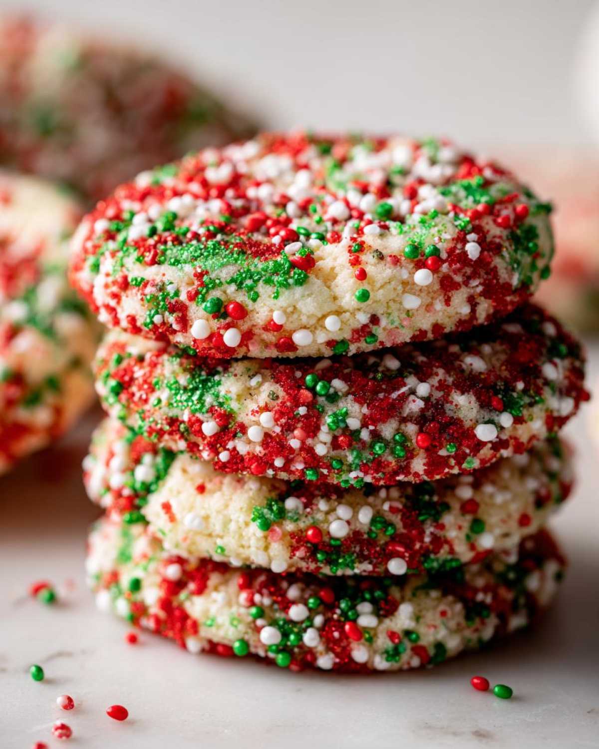 A stack of four delicious christmas sprinkle sugar cookies covered in red, green, and white holiday sprinkles.