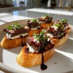 Five pieces of steak crostini bites topped with seared steak, white cheese, and greens, drizzled with balsamic glaze.