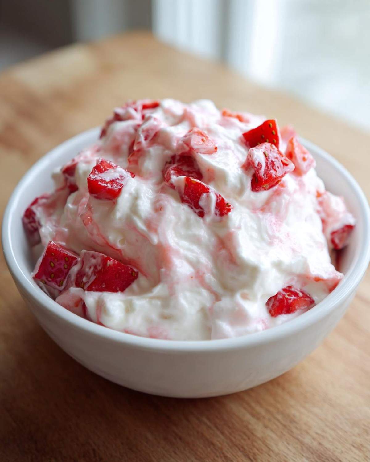 A white bowl filled with creamy strawberry cheesecake dip topped with chunks of fresh, red strawberries.