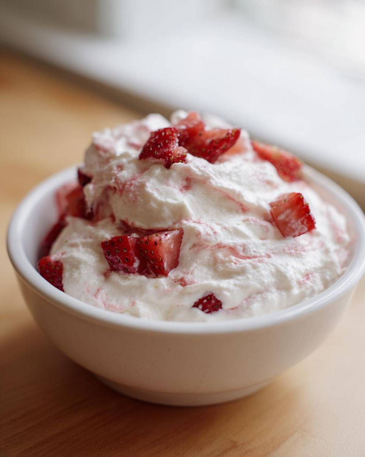 Close-up of creamy strawberry cheesecake dip topped with fresh, diced strawberries in a white bowl.