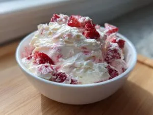 A white bowl filled with fluffy strawberry cheesecake dip topped with fresh, chopped strawberries.