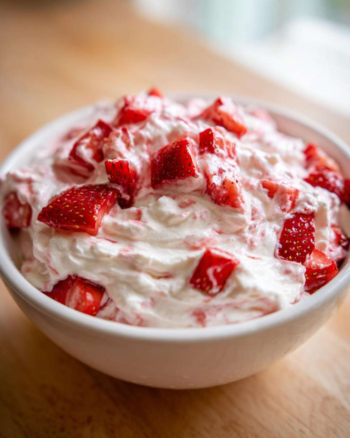 A white bowl filled with creamy strawberry cheesecake dip topped with fresh, diced strawberries.