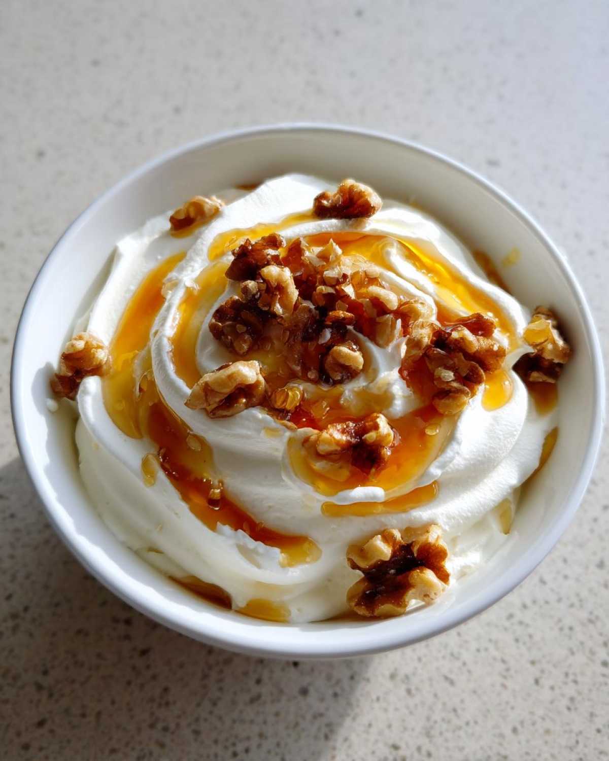 A close-up of a bowl of sweet whipped ricotta dip, drizzled with honey and topped with chopped walnuts.