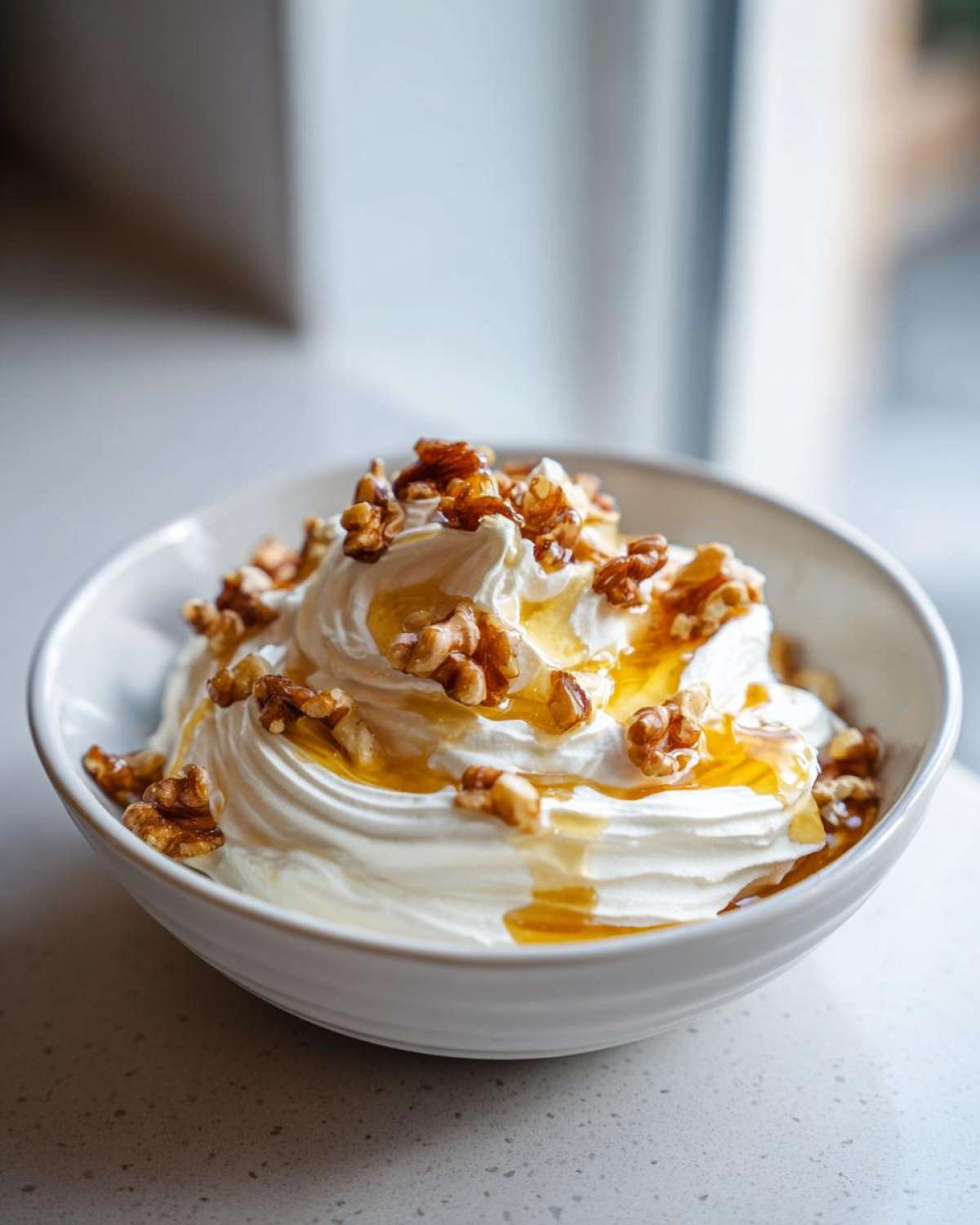 A close-up of creamy whipped ricotta dip swirled high in a white bowl, drizzled with honey and topped with walnuts.