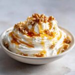 A close-up of a creamy, fluffy whipped ricotta dip topped with whole walnuts and drizzled generously with golden honey.