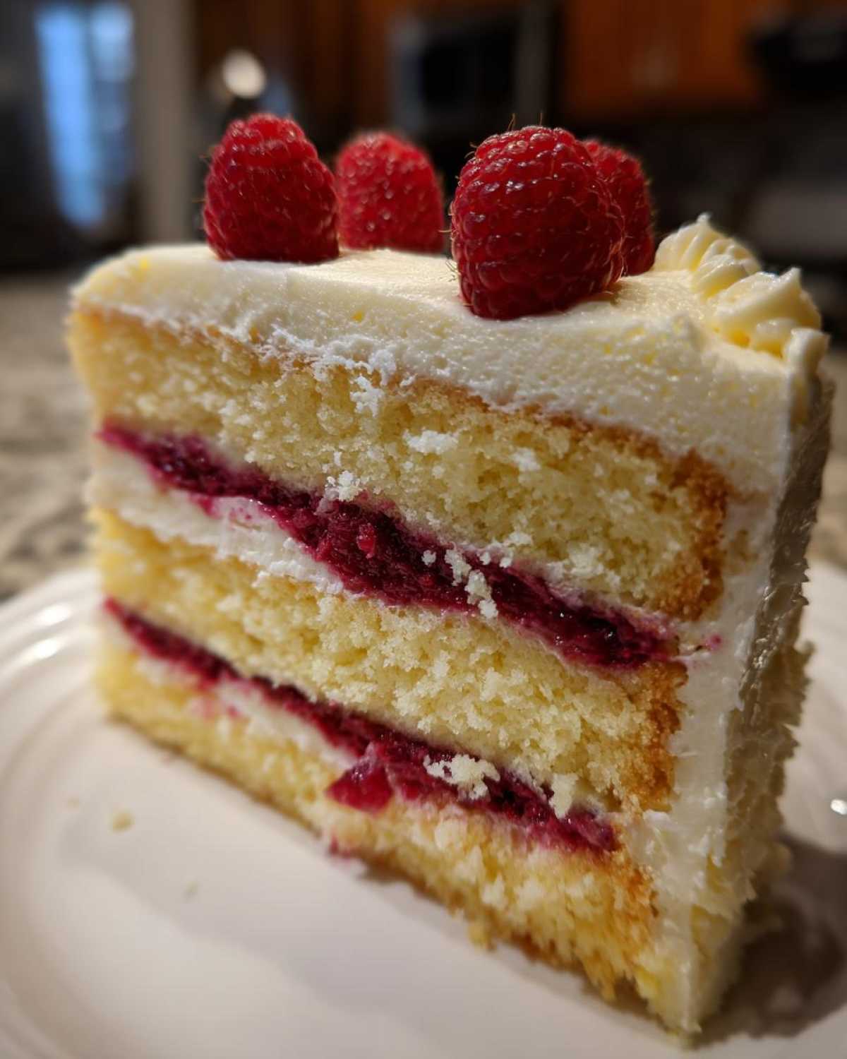 Close-up of a layered slice of white chocolate raspberry cake topped with fresh raspberries.