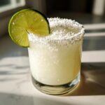 A frosty white Christmas margarita in a rocks glass, garnished with a lime wheel and a shredded coconut rim.