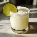 A frosty white Christmas margarita in a rocks glass, garnished with a lime wheel and a shredded coconut rim.