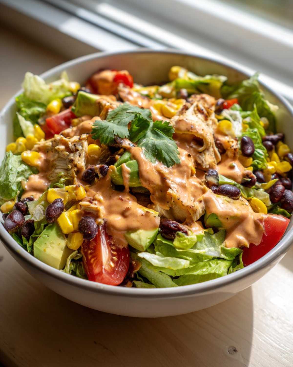 Close-up of a vibrant southwest salad featuring chicken, avocado, black beans, corn, tomatoes, and creamy dressing.