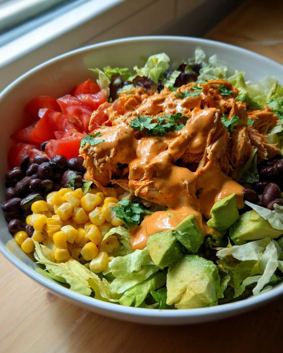 A vibrant bowl of southwest salad featuring shredded chicken topped with orange dressing, avocado, corn, black beans, and tomatoes.