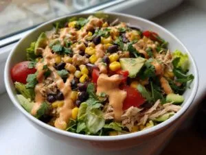 Close-up of a vibrant southwest salad featuring shredded chicken, black beans, corn, avocado, and a creamy orange dressing.