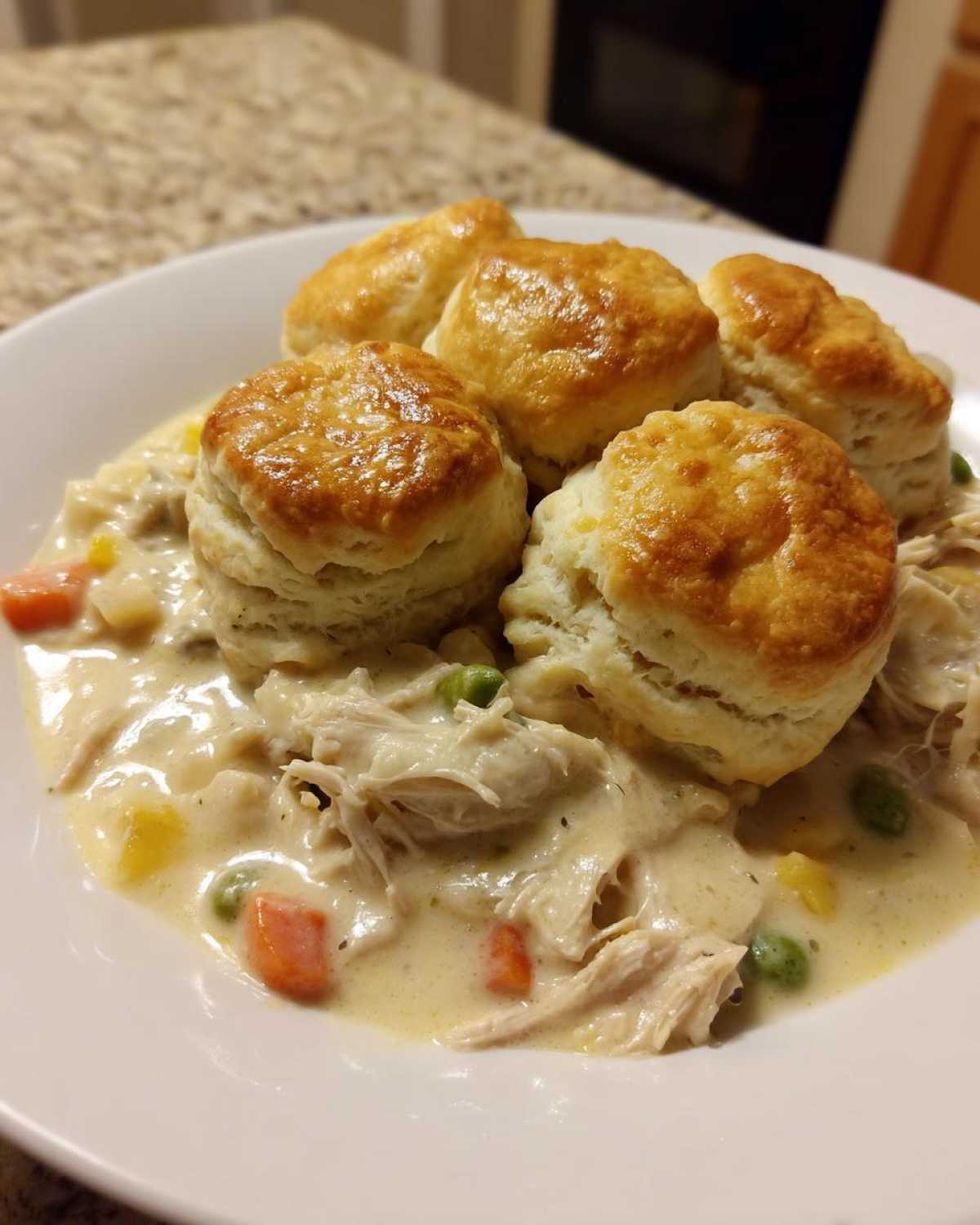 A bowl of creamy chicken pot pie filling topped with four golden brown biscuits.