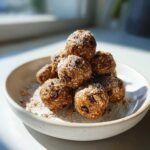 A stack of homemade chocolate chip protein balls coated in coconut flakes, sitting on a light bowl.