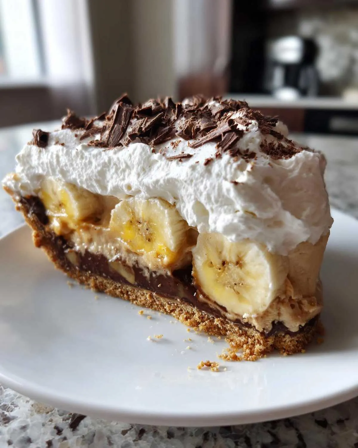 A decadent slice of banoffee pie featuring a graham cracker crust, chocolate, banana slices, and whipped cream topped with chocolate shavings.