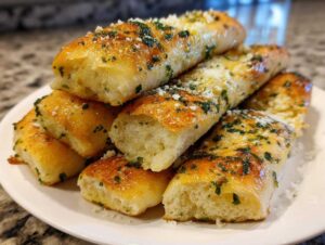 A pile of soft, golden-brown breadsticks brushed with garlic butter, topped with grated Parmesan and parsley.