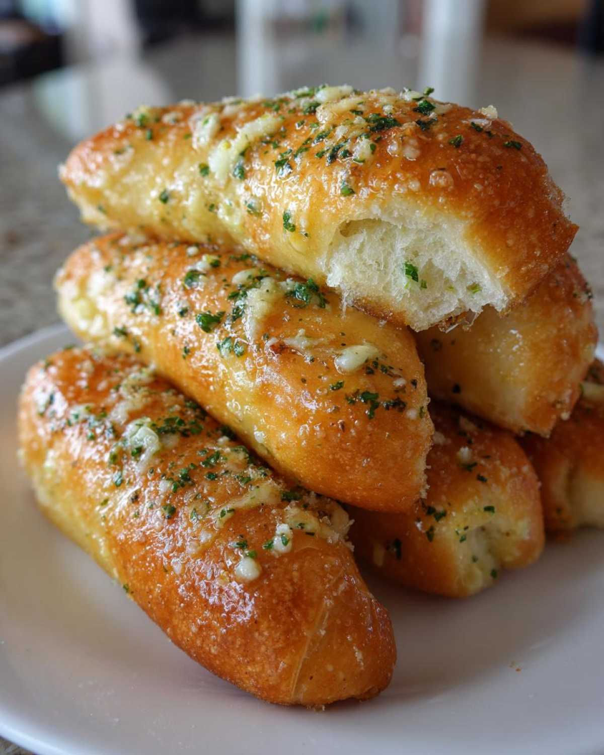 A stack of soft, golden-brown garlic breadsticks topped with melted butter, Parmesan cheese, and parsley.