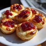 Close-up of several golden baked brie bites topped with melted brie and bright red raspberry jam.