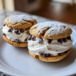 Two delicious cannoli cookies sandwiched with sweet cream filling and mini chocolate chips, dusted with powdered sugar.