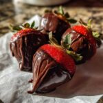 Close-up of four fresh chocolate covered strawberries sitting on white parchment paper.