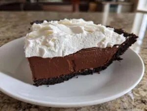 A decadent slice of chocolate cream pie featuring a dark chocolate crust, rich filling, and thick whipped topping.