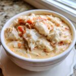 Close-up of a white bowl filled with rich, creamy crab soup topped with large chunks of white and orange crab meat.