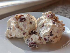Two scoops of creamy, white cranberry salad mixed with dried cranberries and walnuts on a white plate.