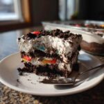 A generous slice of no-bake dirt cake featuring layers of chocolate crumbs, white cream, and colorful gummy worms.