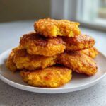 A stack of perfectly golden brown hot water cornbread patties piled high on a white plate.