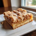 Close-up of a single serving of apple pie bars with a thick layer of spiced apples, crumb topping, and vanilla glaze.