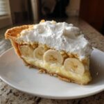 A close-up of a slice of amazing banana cream pie with layers of custard, banana slices, and whipped cream.