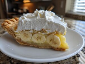 A close-up of a slice of amazing banana cream pie with layers of crust, sliced bananas, custard, and whipped cream.