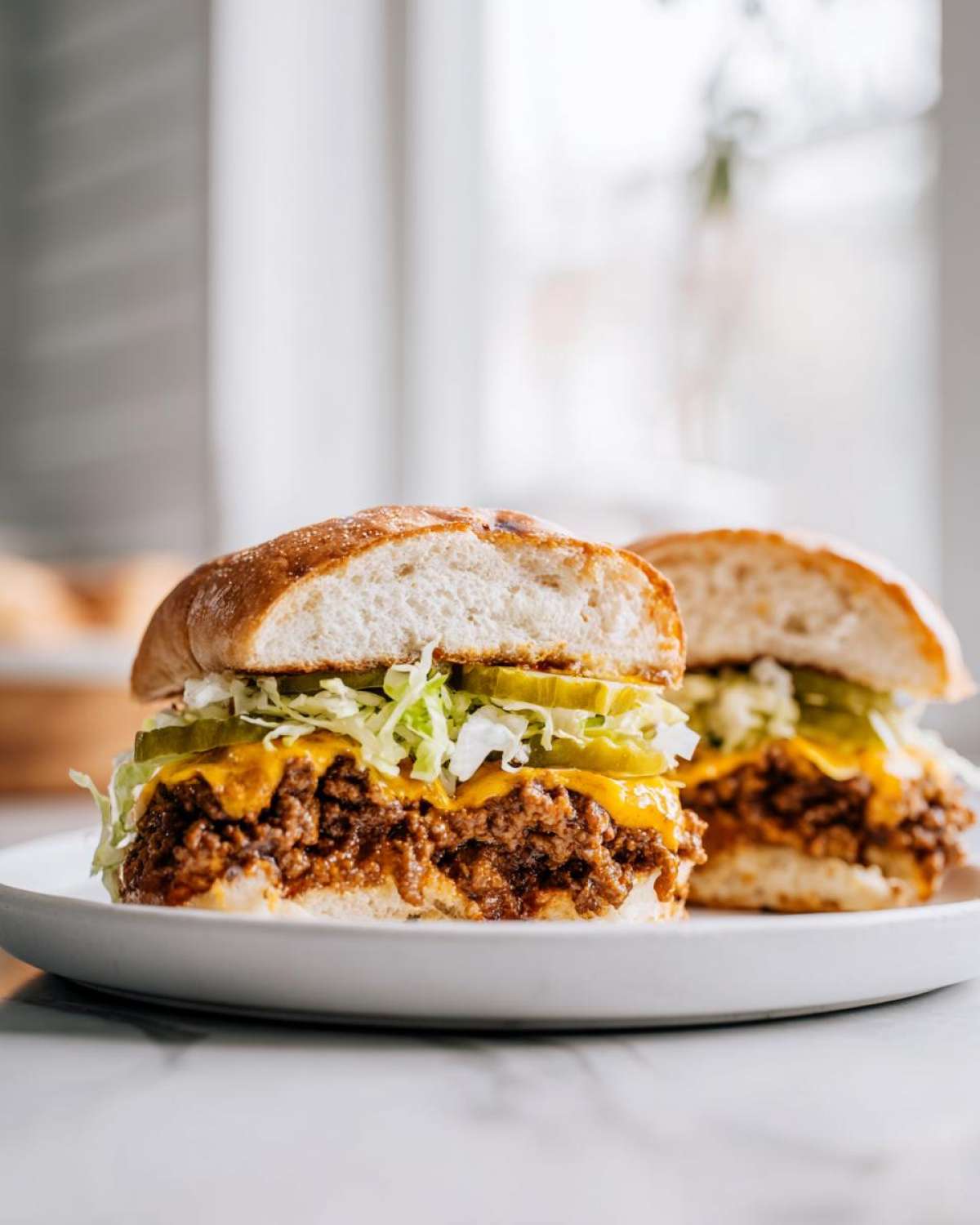 Two halves of a big mac sloppy joes sandwich stacked with ground beef, cheese, lettuce, and pickles on a white plate.