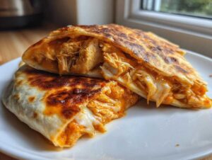 Close-up of a golden-brown buffalo chicken quesadilla cut in half, showing shredded chicken and melted cheese.